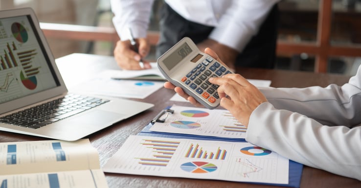 two people at a table with graphs, a calculator, paper and a computer 